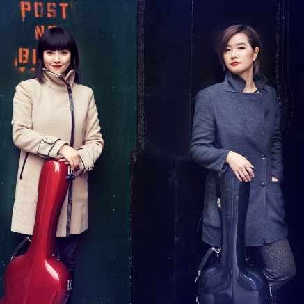 Beijing Guitar Duo Standing next to each other, one in a tan coat with a red case and one in a long, black coat with a black case