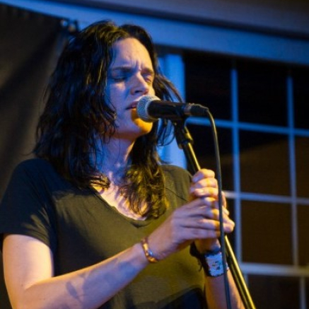 Image of Leanne Simpson speaking into a microphone. She has dark hair and is wearing a black t-shirt.